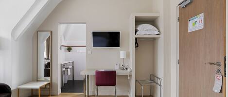 A compact hotel room with a desk, chair, and a television.