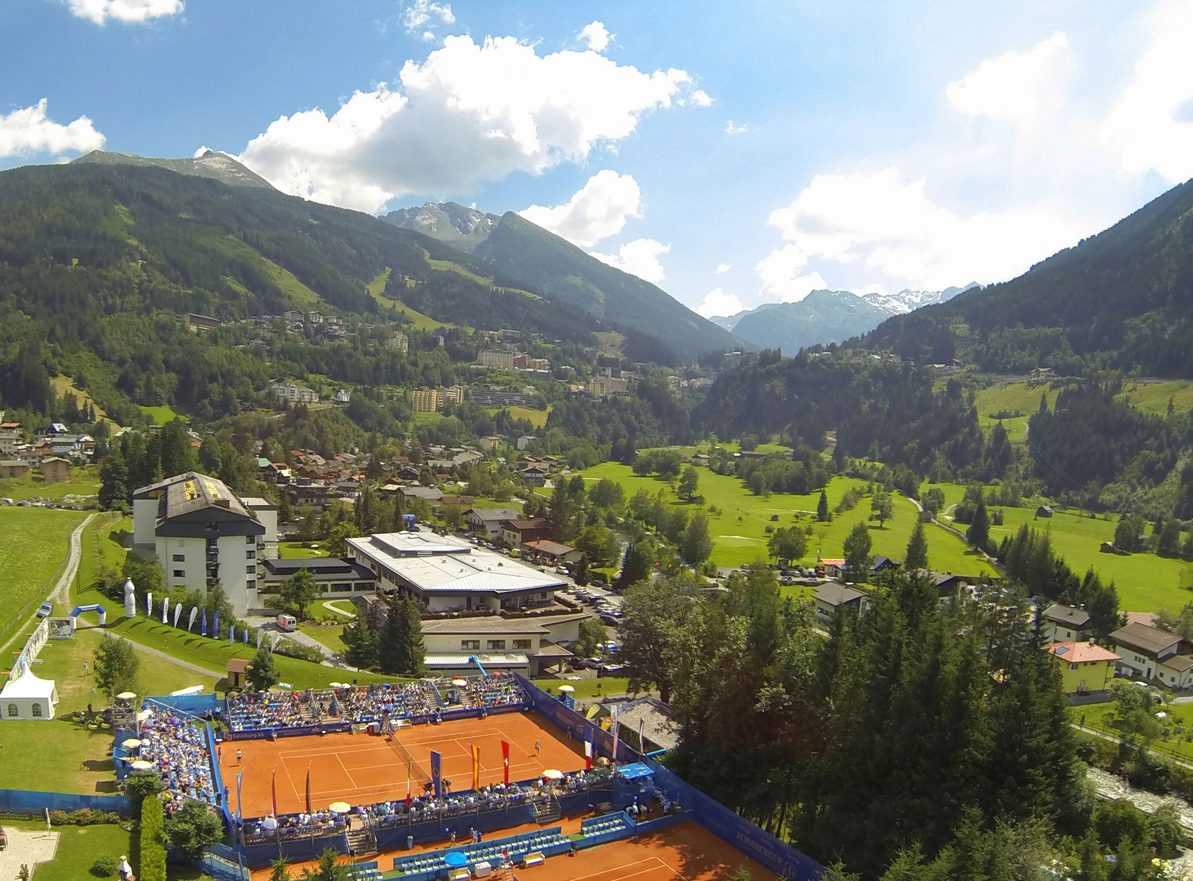 A tennis court surrounded by a mountainous landscape with a town in the background.