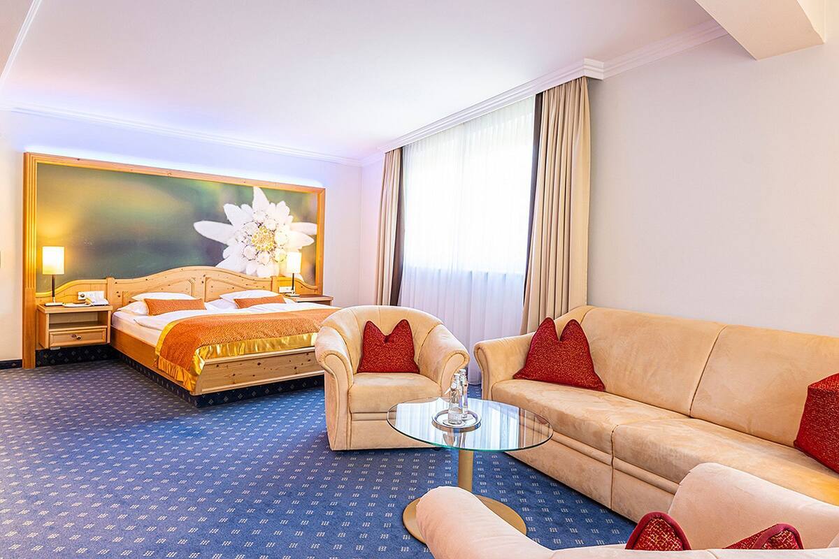 Une chambre d’hôtel avec un lit, un canapé, une petite table et une grande fenêtre avec des rideaux.