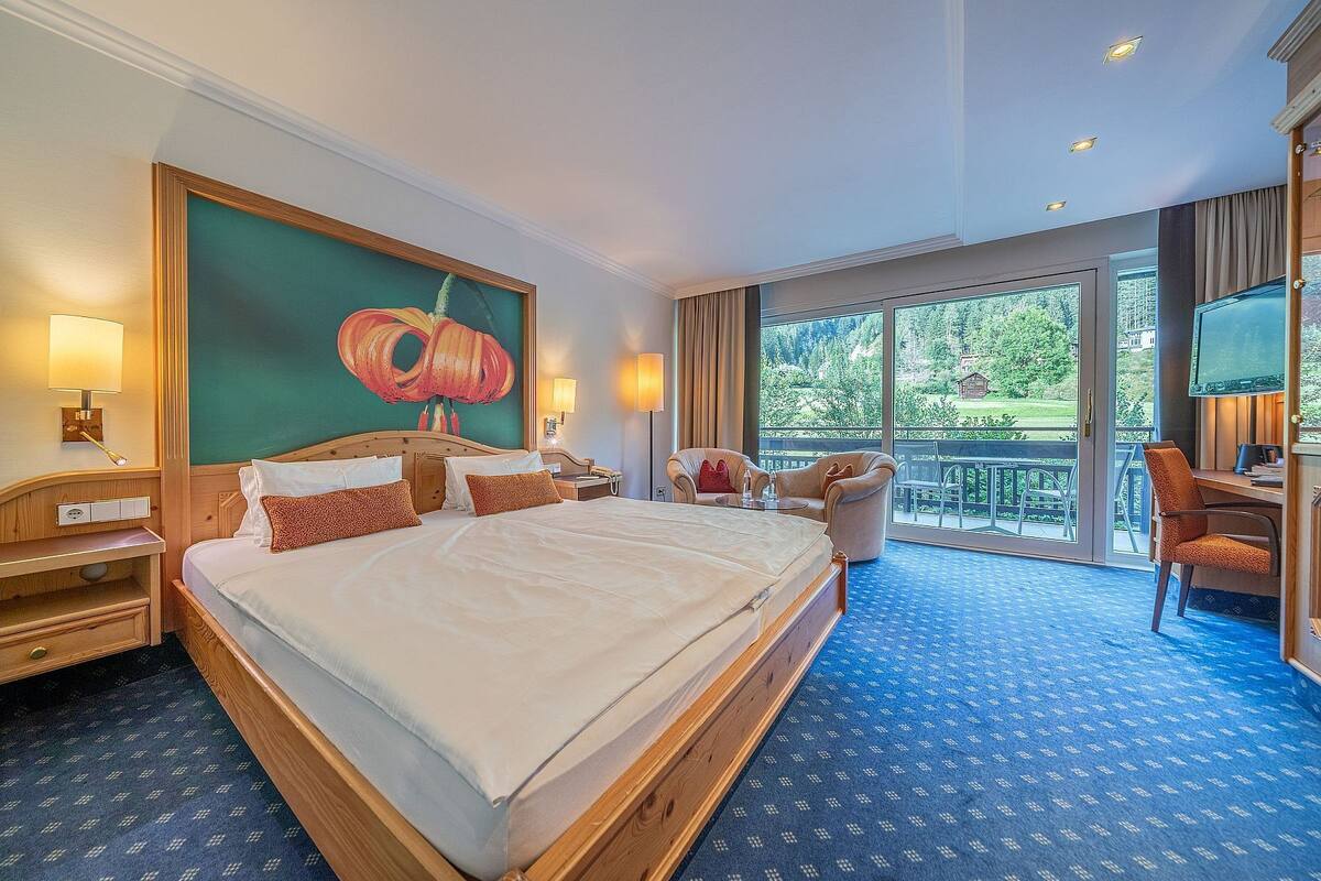Une chambre d’hôtel avec un grand lit, un bureau, une chaise, une télévision et un balcon donnant sur un espace verdoyant.
