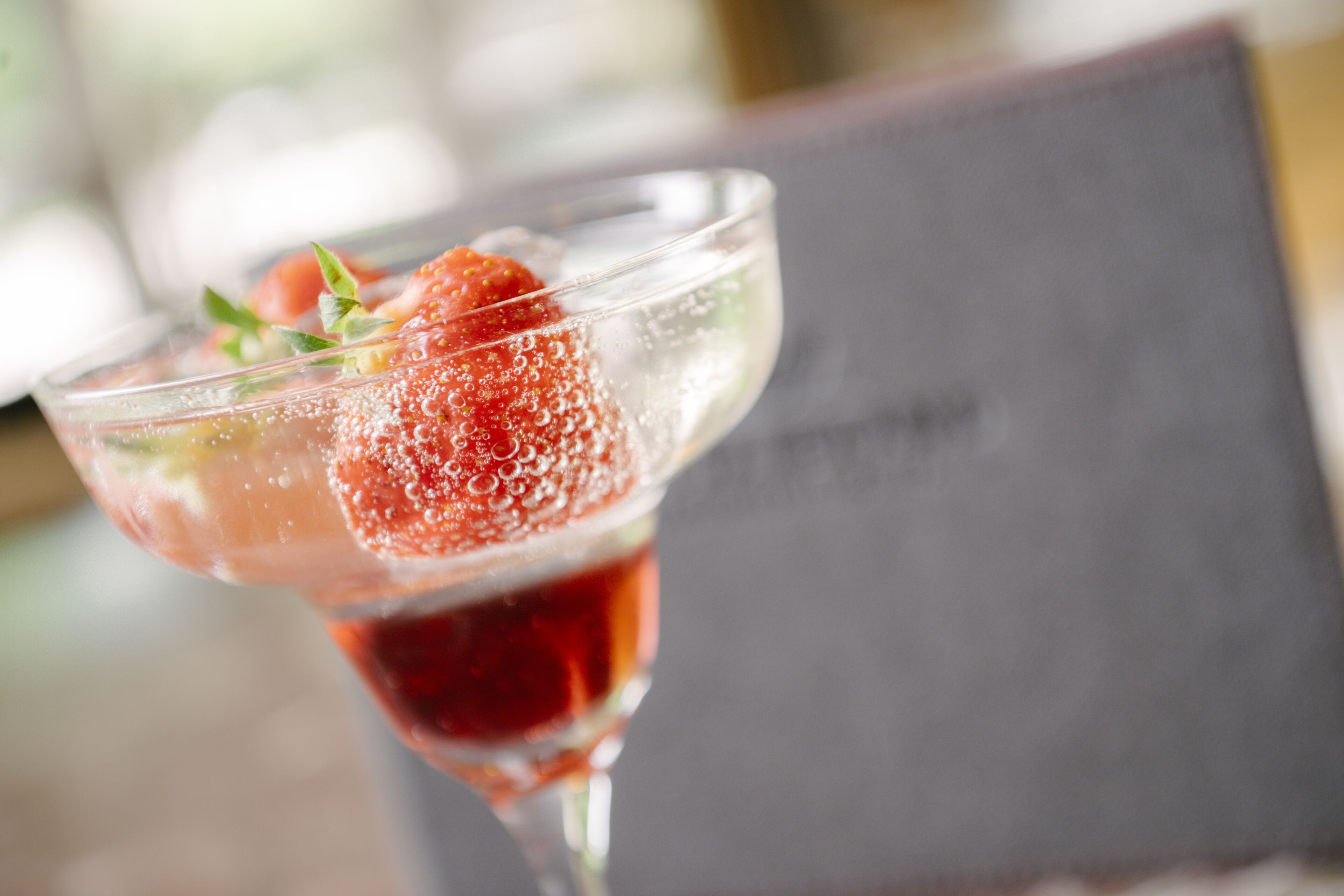 A cocktail glass with a strawberry garnish and ice cubes.