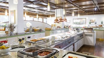 Un bufé con diferentes estaciones de comida, que incluye una barra de ensaladas, una estación de platos calientes y una estación de postres.