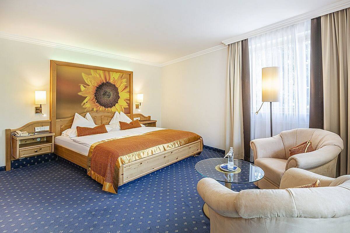 Une chambre d’hôtel avec un grand lit, une petite table, une chaise et une grande fenêtre avec des rideaux.