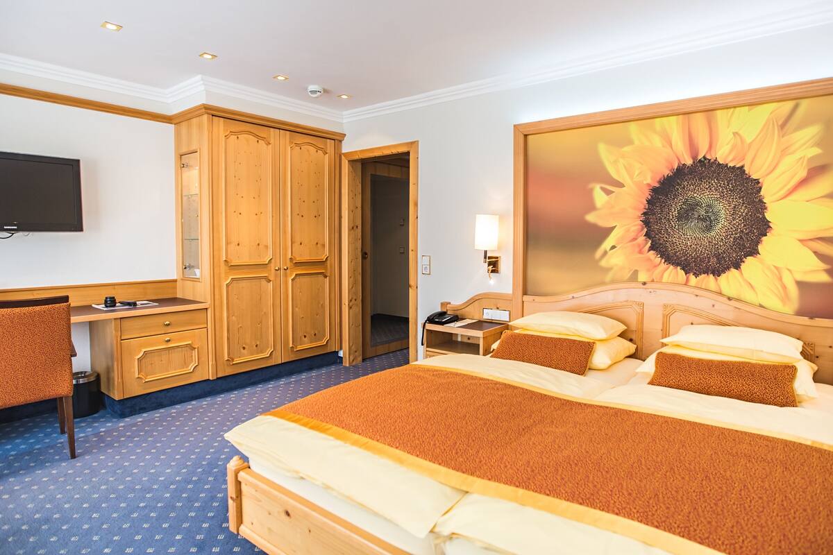 Une chambre d’hôtel avec un grand lit, un bureau, une chaise, une télévision et un mur orné d’un tableau représentant des tournesols.