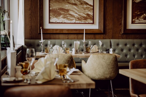 A dining area with a wooden wall, a cushioned bench, and a table set with glasses and candles.