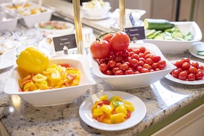 A buffet with various fruits and vegetables, including bell peppers, tomatoes, and cucumbers.