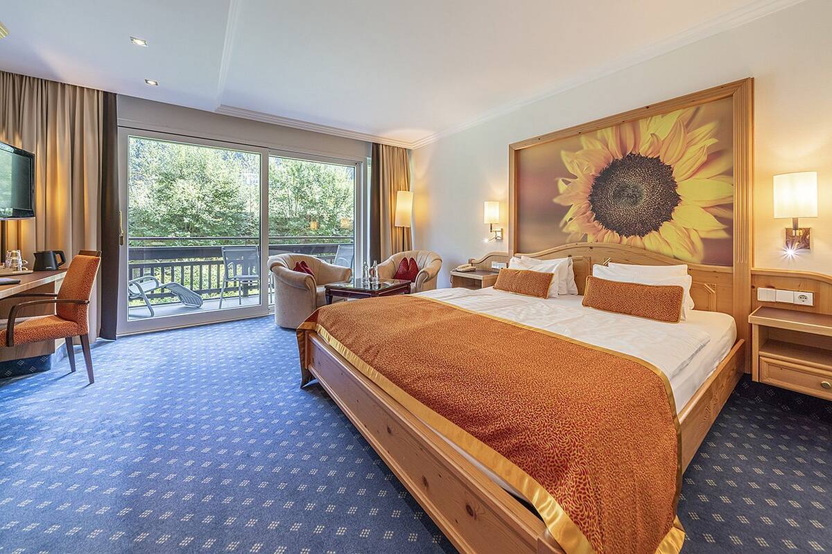 Une chambre d’hôtel avec un grand lit, un bureau, une chaise et un balcon donnant sur la verdure.