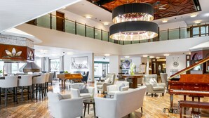 A spacious lobby with a grand piano, comfortable seating, a high ceiling with a chandelier, and a second-floor balcony. - EUROPÄISCHER HOF Bad Gastein (Bad Gastein)