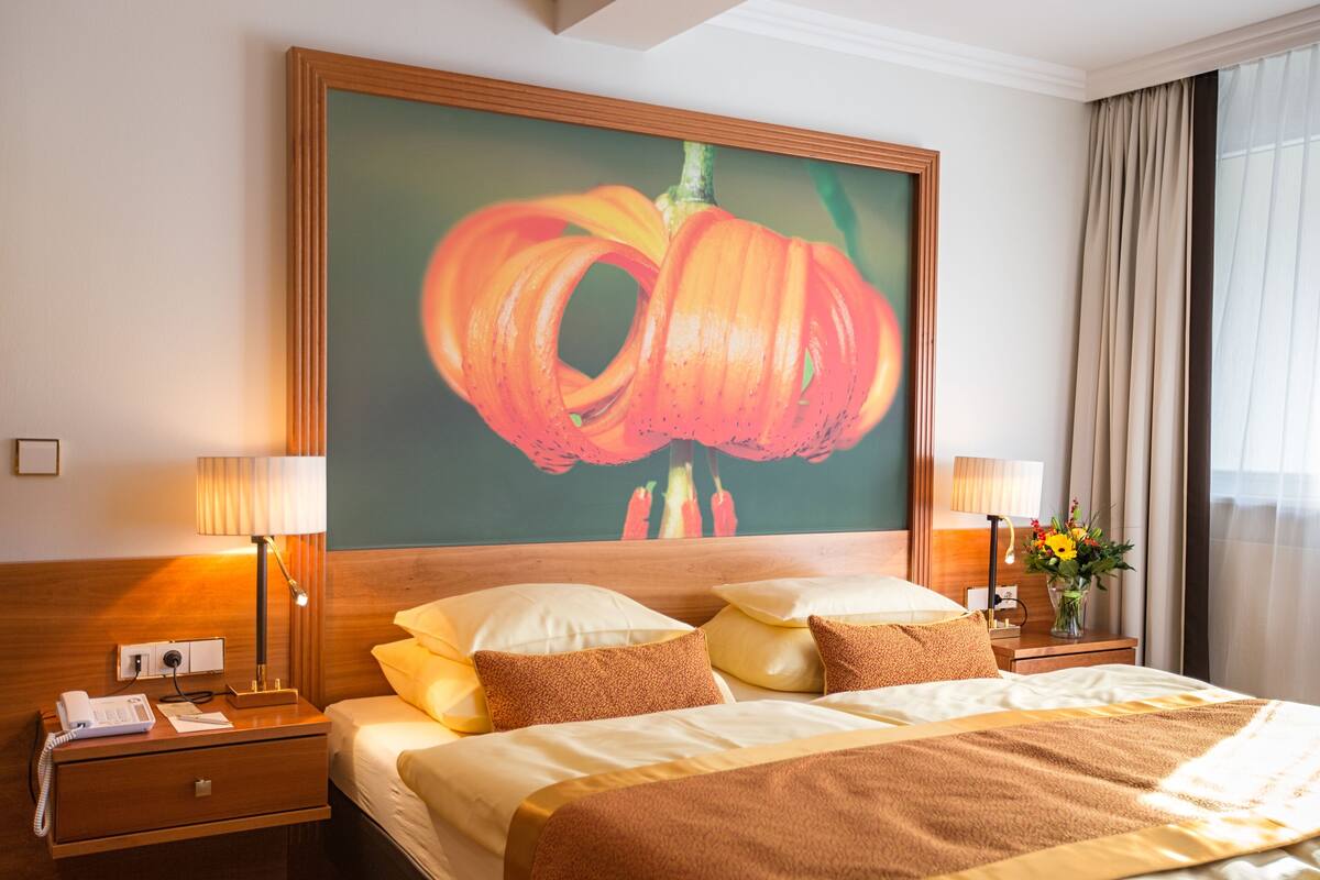 Une chambre d’hôtel avec un grand lit, deux lampes de chevet, une table de chevet avec un téléphone et un tableau représentant une fleur accroché au mur.