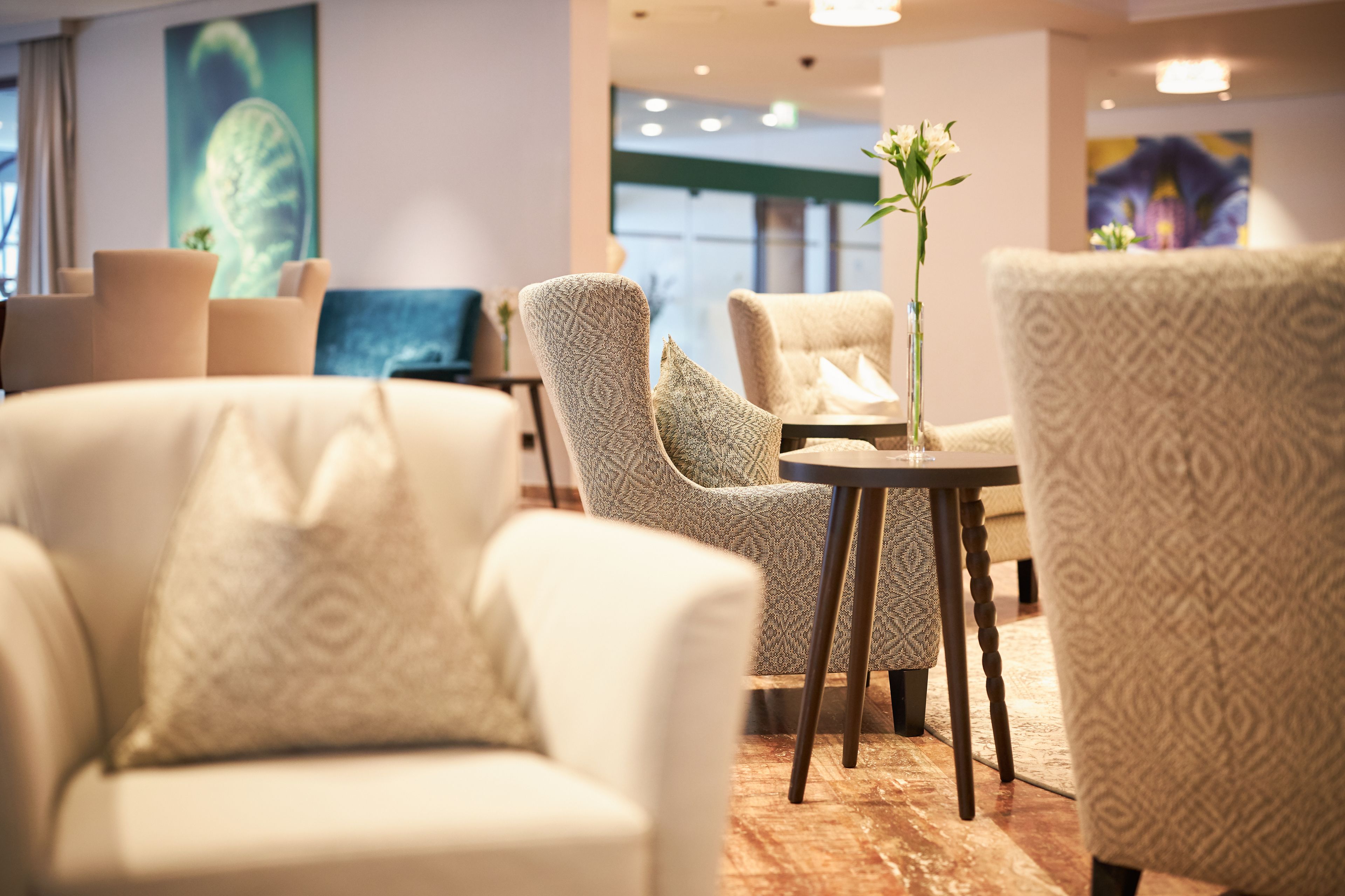 A modern hotel lobby with a seating area featuring patterned armchairs and a small table with a vase of flowers.