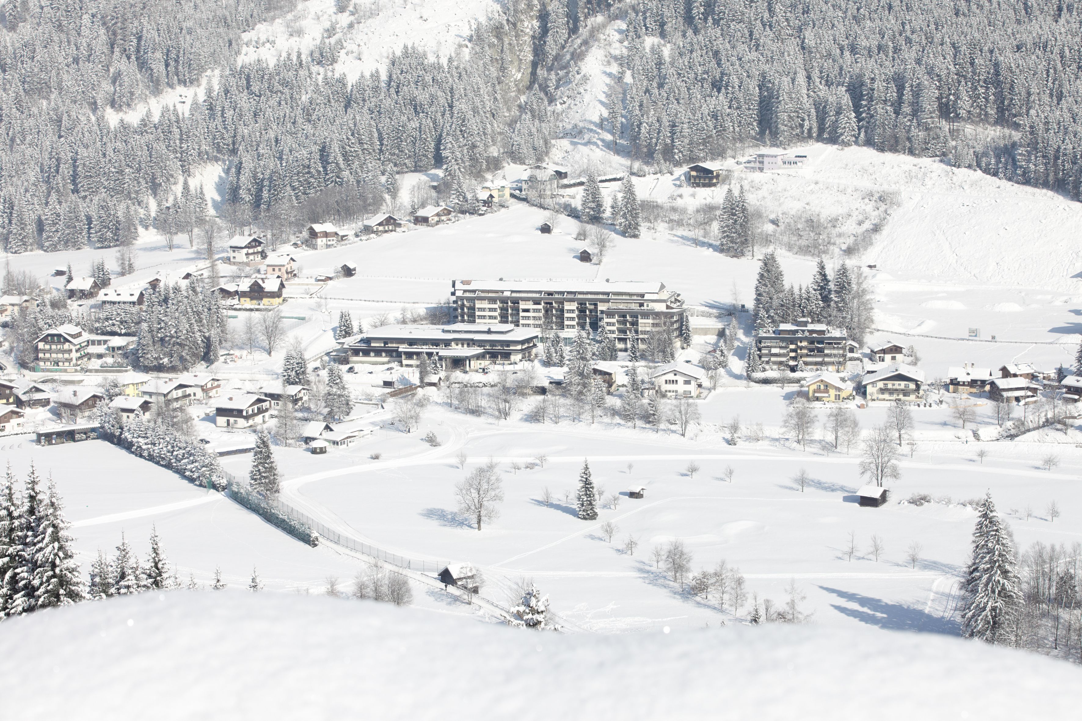 A snow-covered village with multiple buildings, including a large hotel with multiple floors and a smaller lodge nearby.