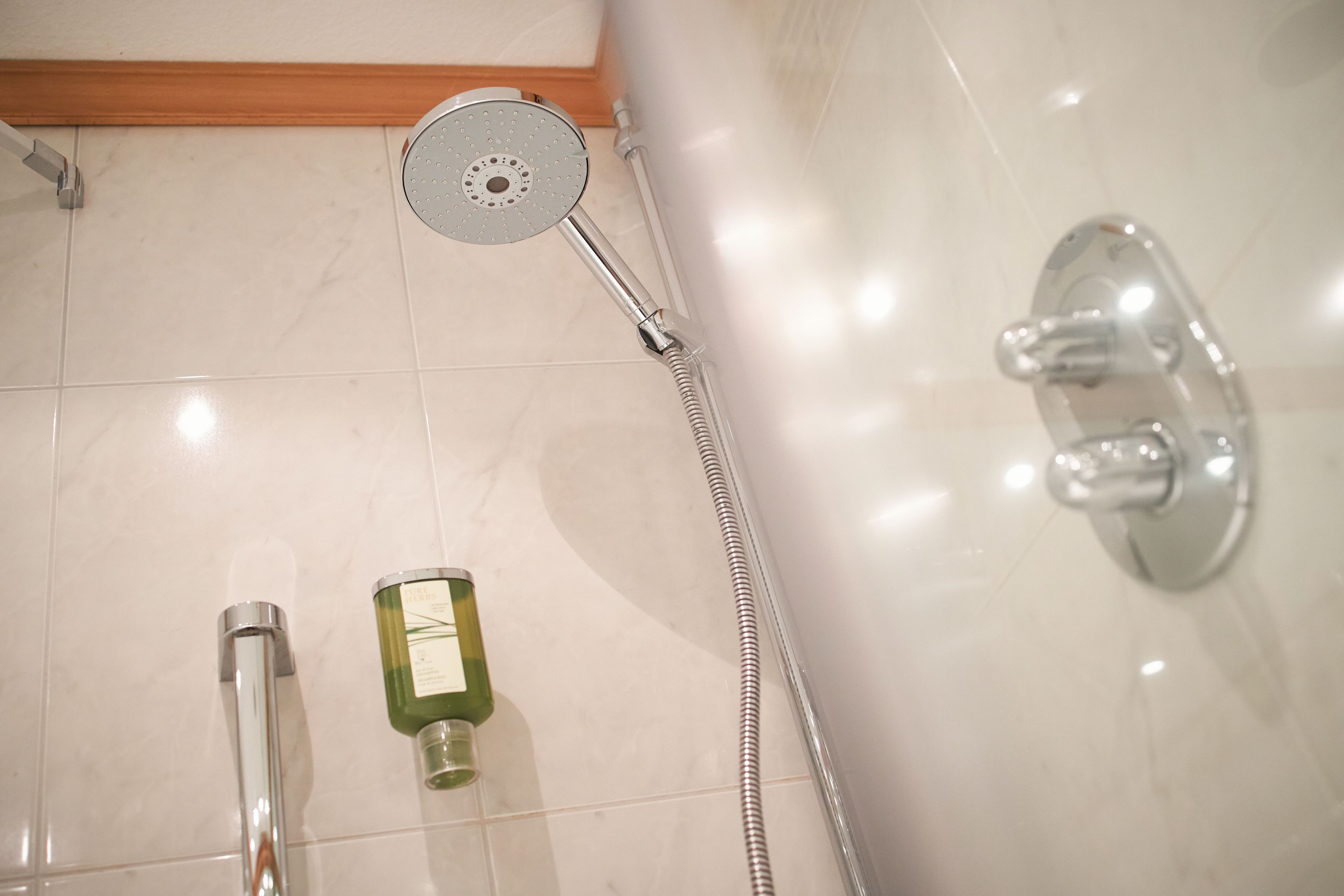 Une salle de bain avec une douche, un pommeau de douche amovible et une bouteille de shampoing.