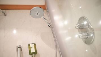 Une salle de bain avec une douche, un pommeau de douche amovible et une bouteille de shampoing.