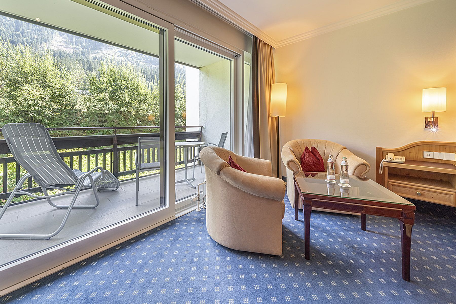 Une chambre d’hôtel avec un balcon, un canapé, une table et une lampe.