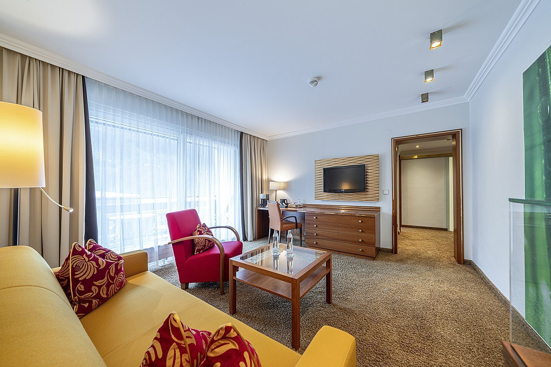 Habitació d'hotel amb sofà, butaca, taula de centre, televisió i escriptori amb làmpada.