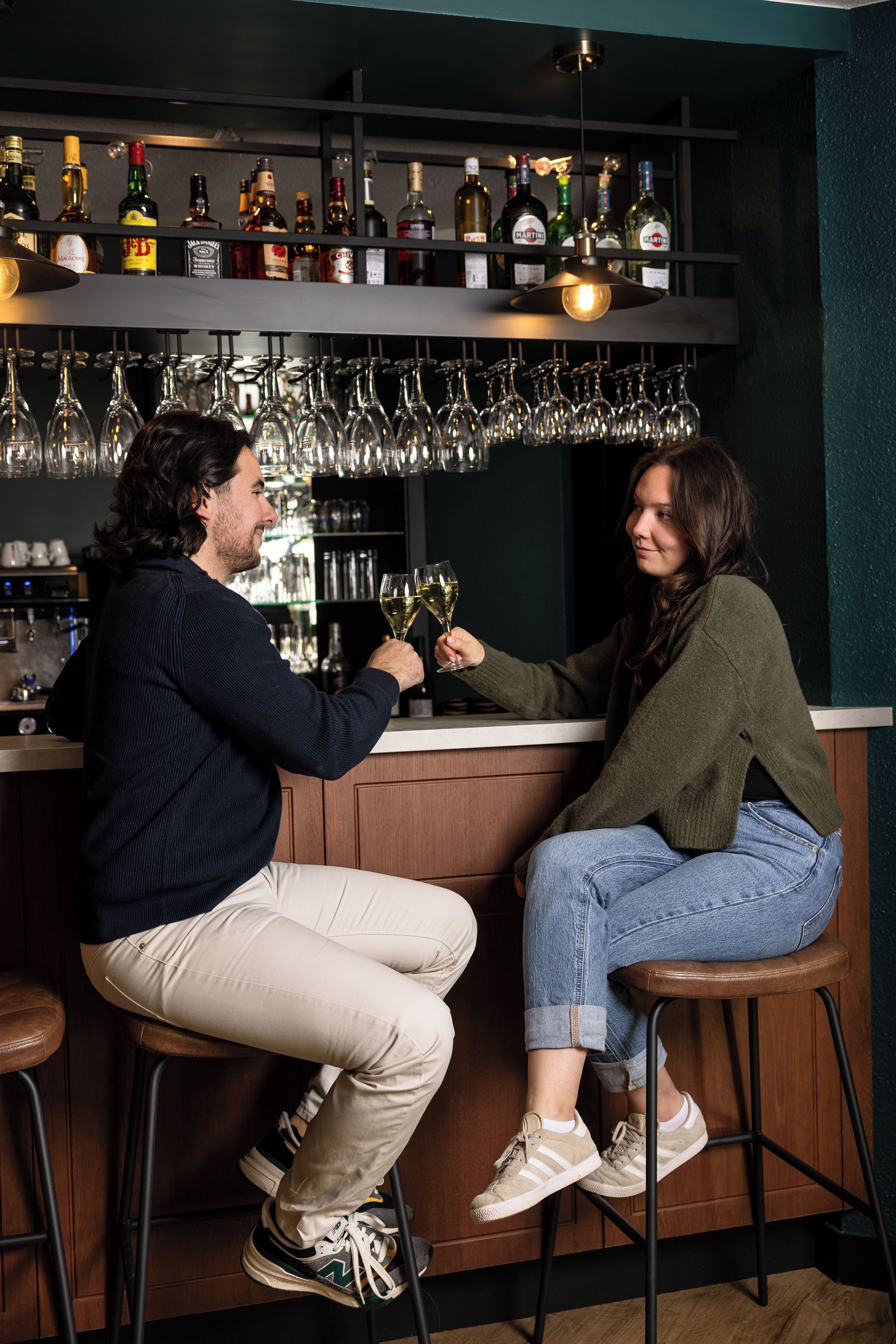 Two people sitting at a bar with a variety of bottles and glasses behind them.