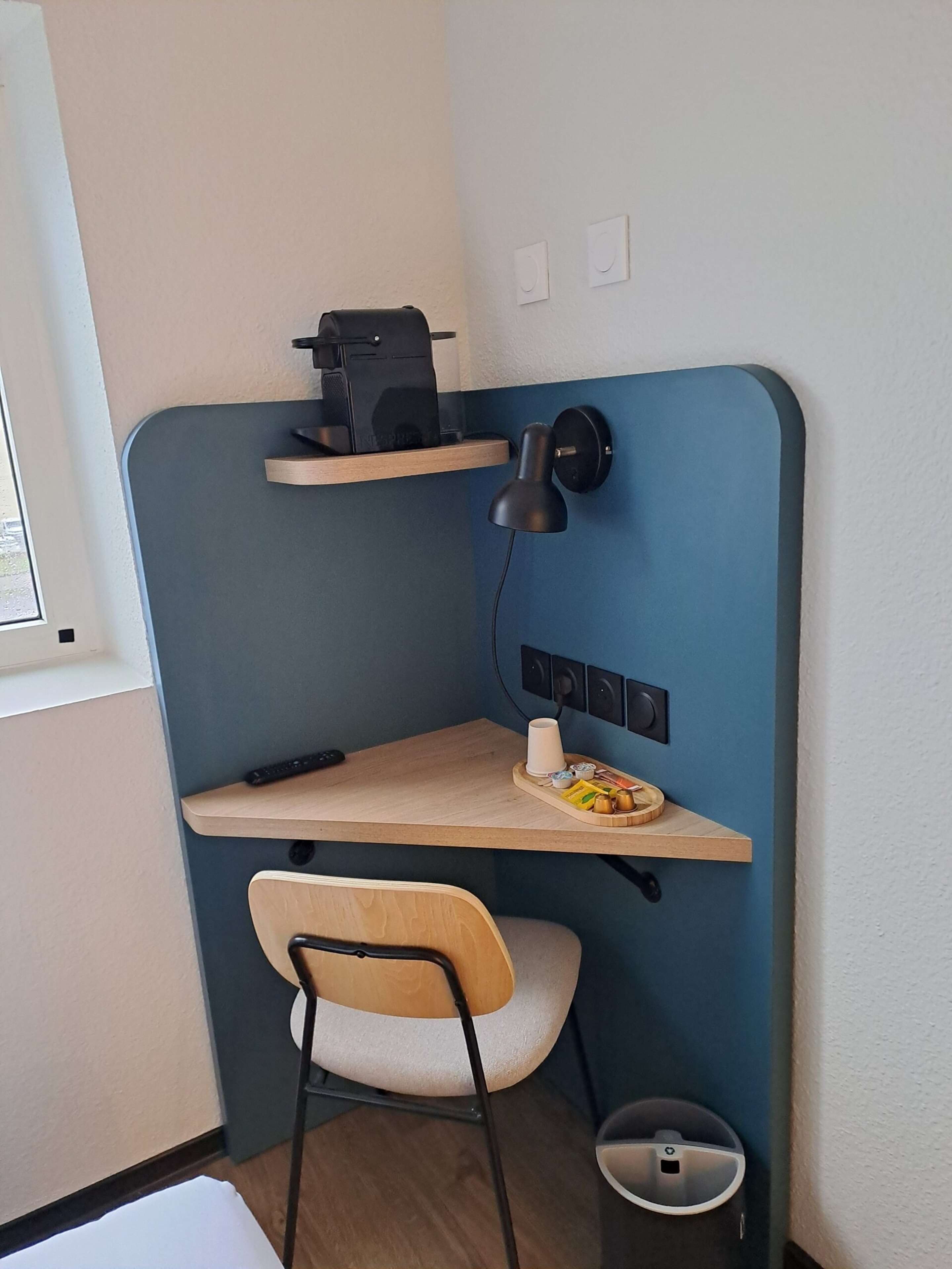 Um espaço de trabalho pequeno e funcional, com escrivaninha, cadeira e máquina de café.
