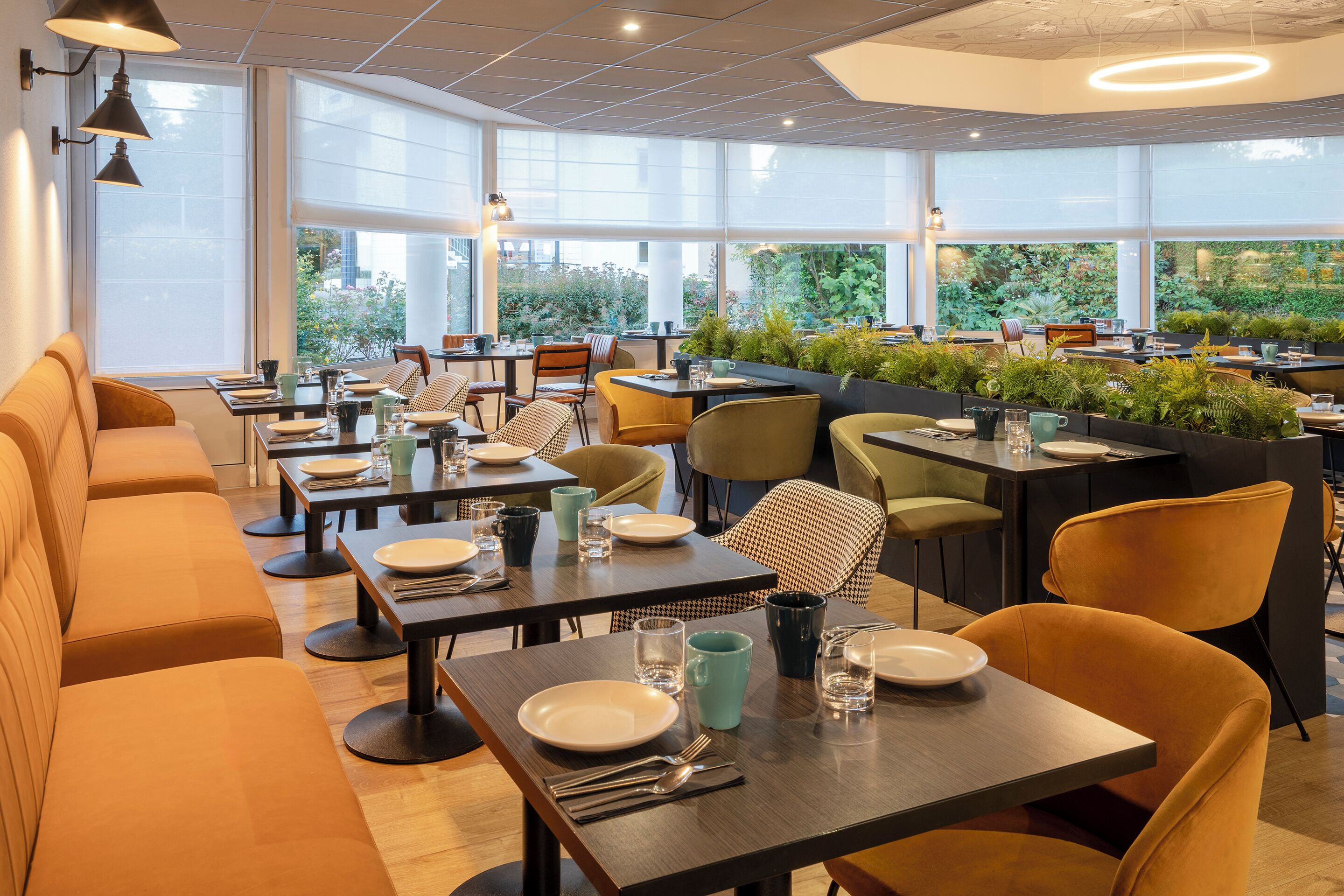 Un restaurante moderno con varias mesas y reservados, ventanas amplias y plantas de interior.