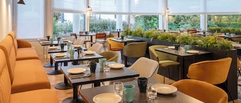 Un restaurante moderno con varias mesas y reservados, ventanas amplias y plantas de interior.