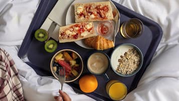 Bandeja de desayuno con tostadas, fruta, cereal y jugo sobre la cama.