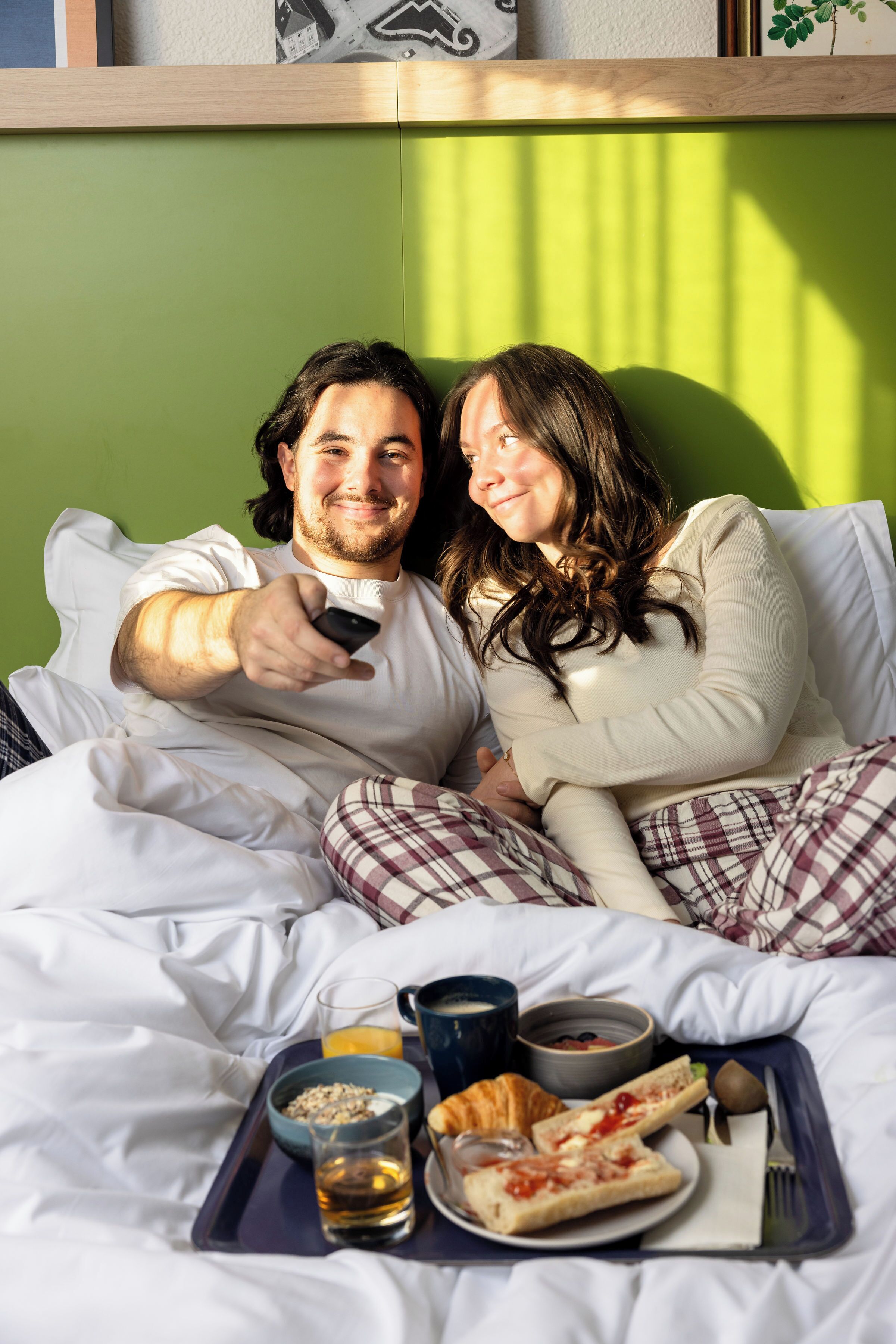 Una pareja en una cama con artículos de desayuno, como croissants, cereal y bebidas.