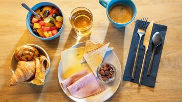 Een ontbijttafel met croissants, kaas, ham, toast, fruit, noten, koffie en thee.
