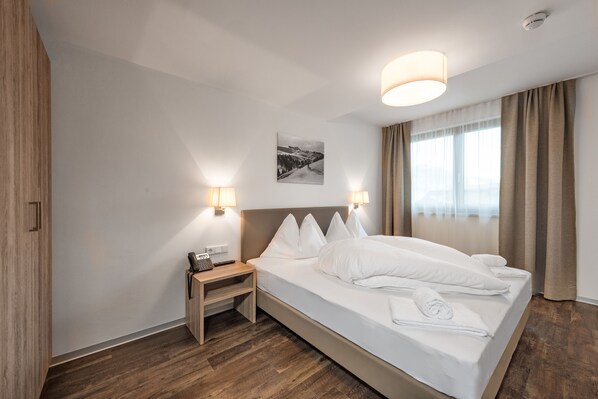 Habitación de hotel con una cama grande, lámparas de noche, una mesita con un teléfono y un cuadro en la pared.