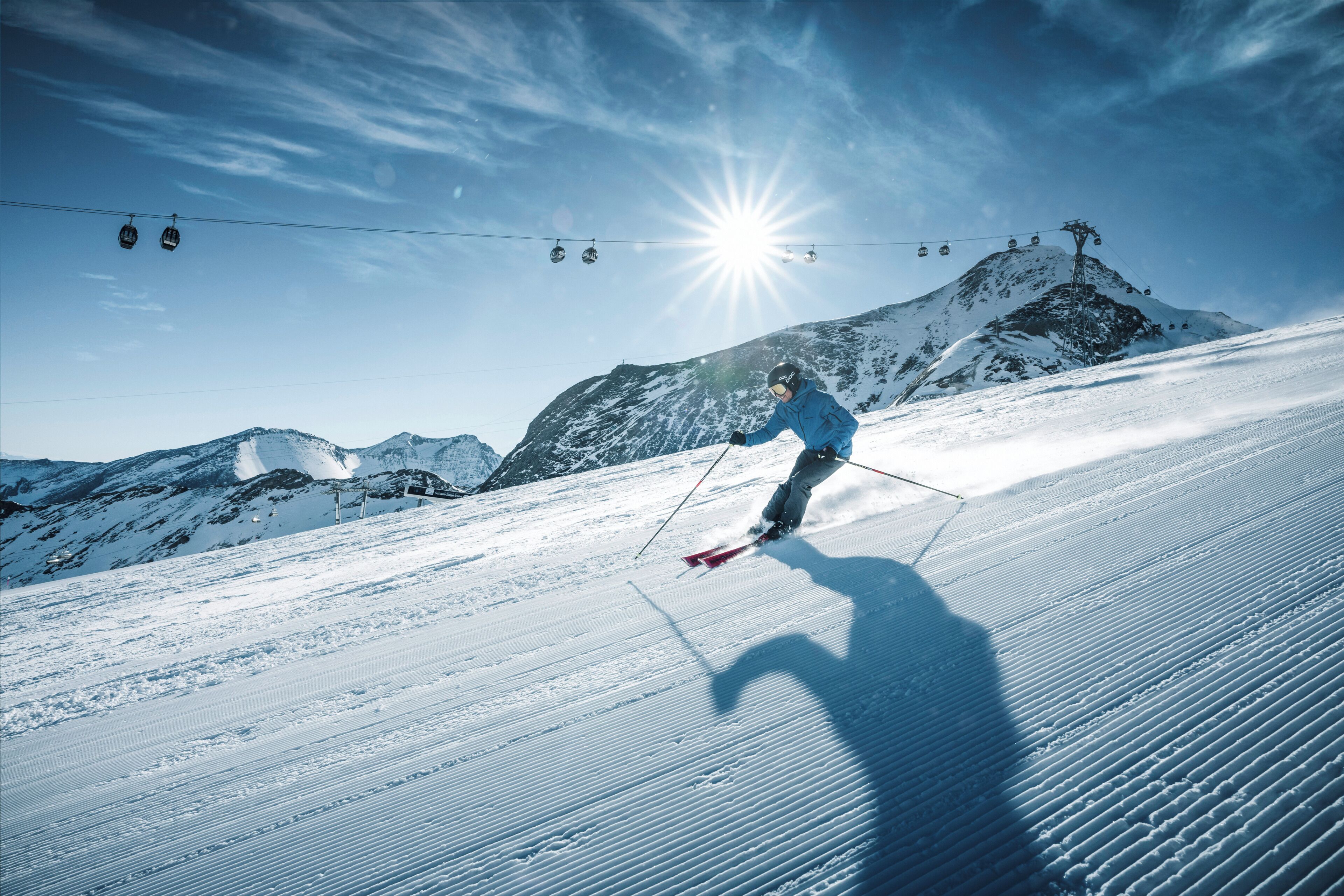 A skier on a snowy slope with a clear sky and a sun in the background.