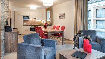 A modern living room with a grey sofa, red chairs, a wooden coffee table, and a view of the kitchen and dining area.