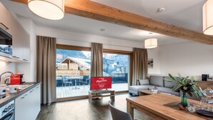 Eine moderne Küche mit Holzboden, ein Essbereich mit Holztisch und -stühlen sowie ein Blick auf Berge durch große Fenster.