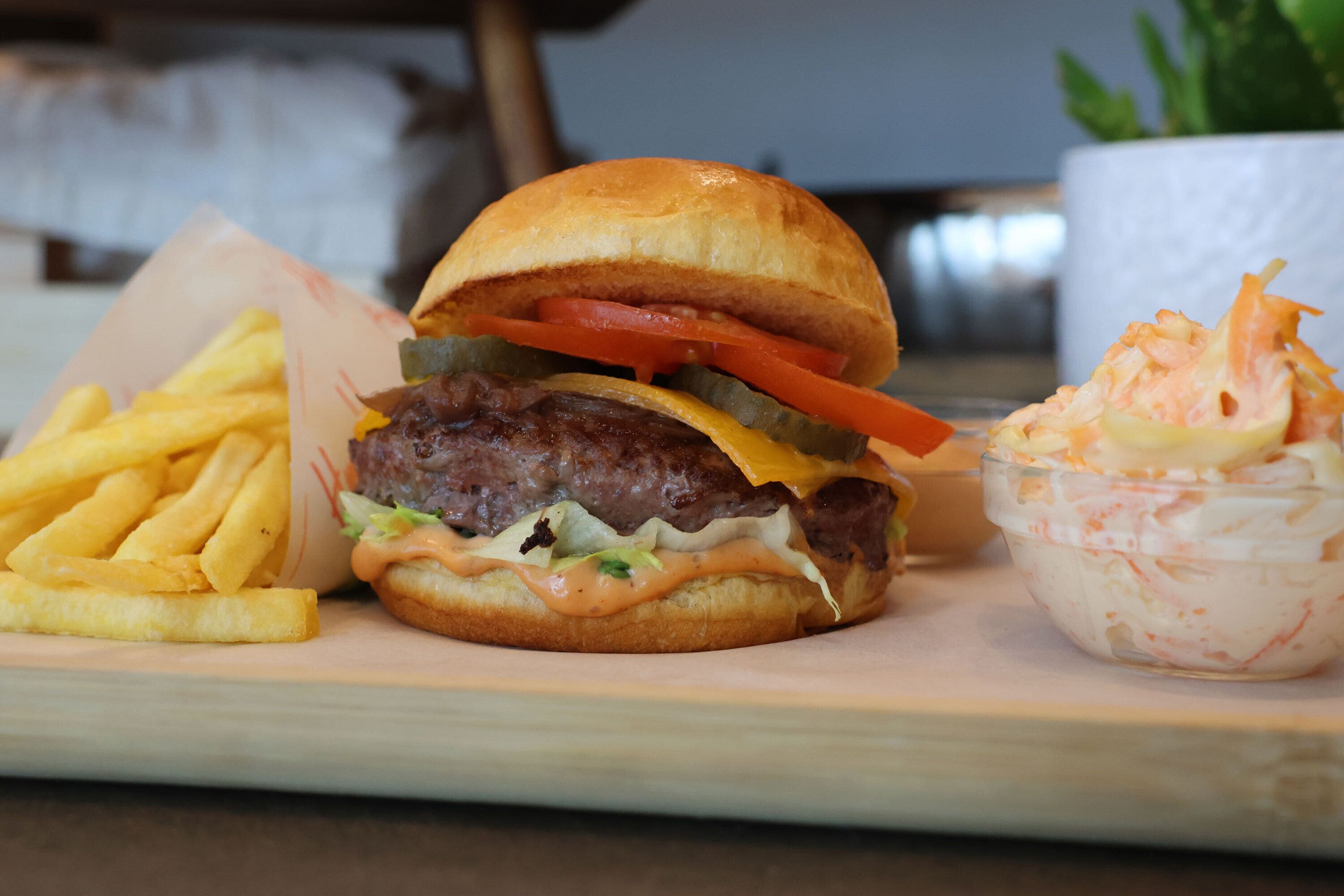 Un hamburger accompagné de frites et d’une salade, le tout servi sur une planche en bois.