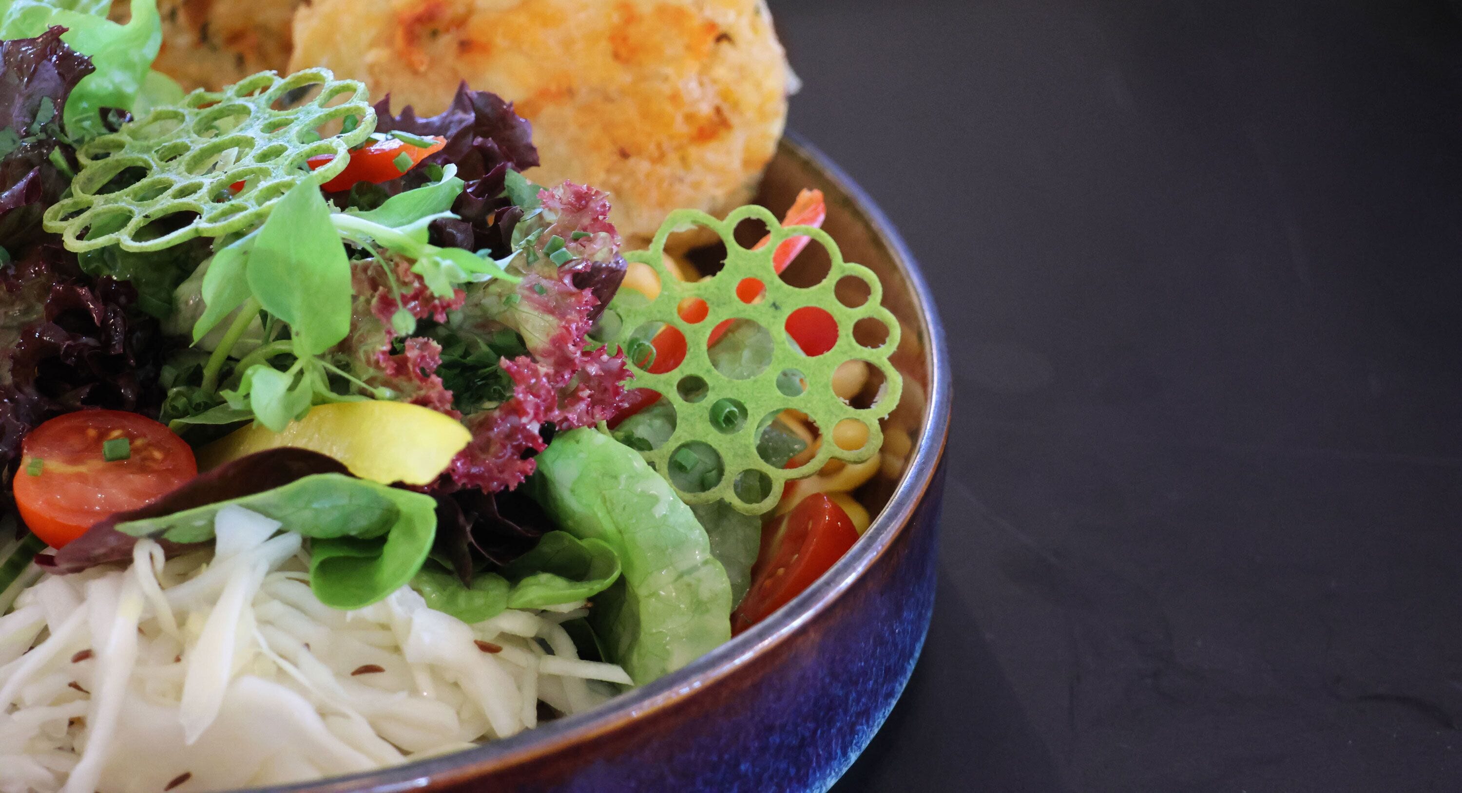 A bowl of salad with various vegetables and a biscuit.