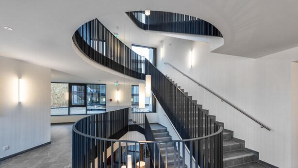 Ein modernes Interieur mit einer geschwungenen Treppe, großen Fenstern und einer Sitzecke mit einer Lampe.