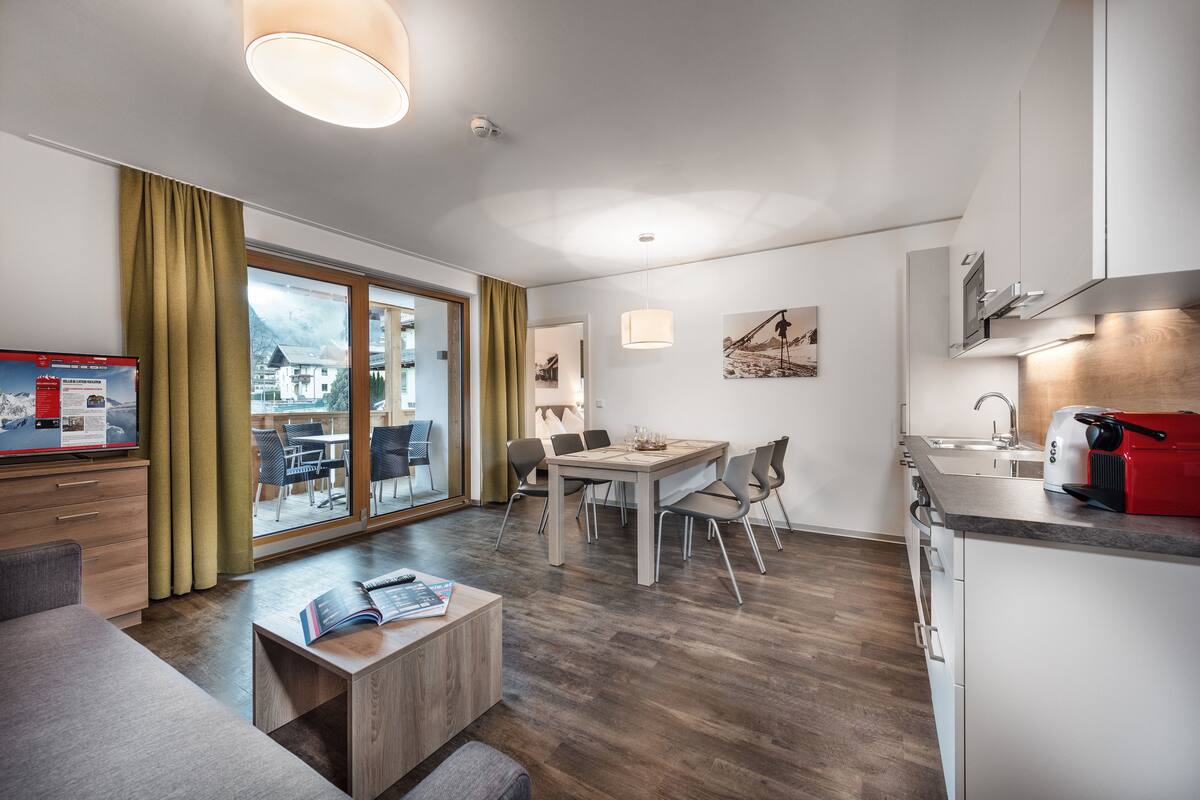 Una habitación de hotel moderna con comedor, cocina y un amplio ventanal con vistas a la montaña.