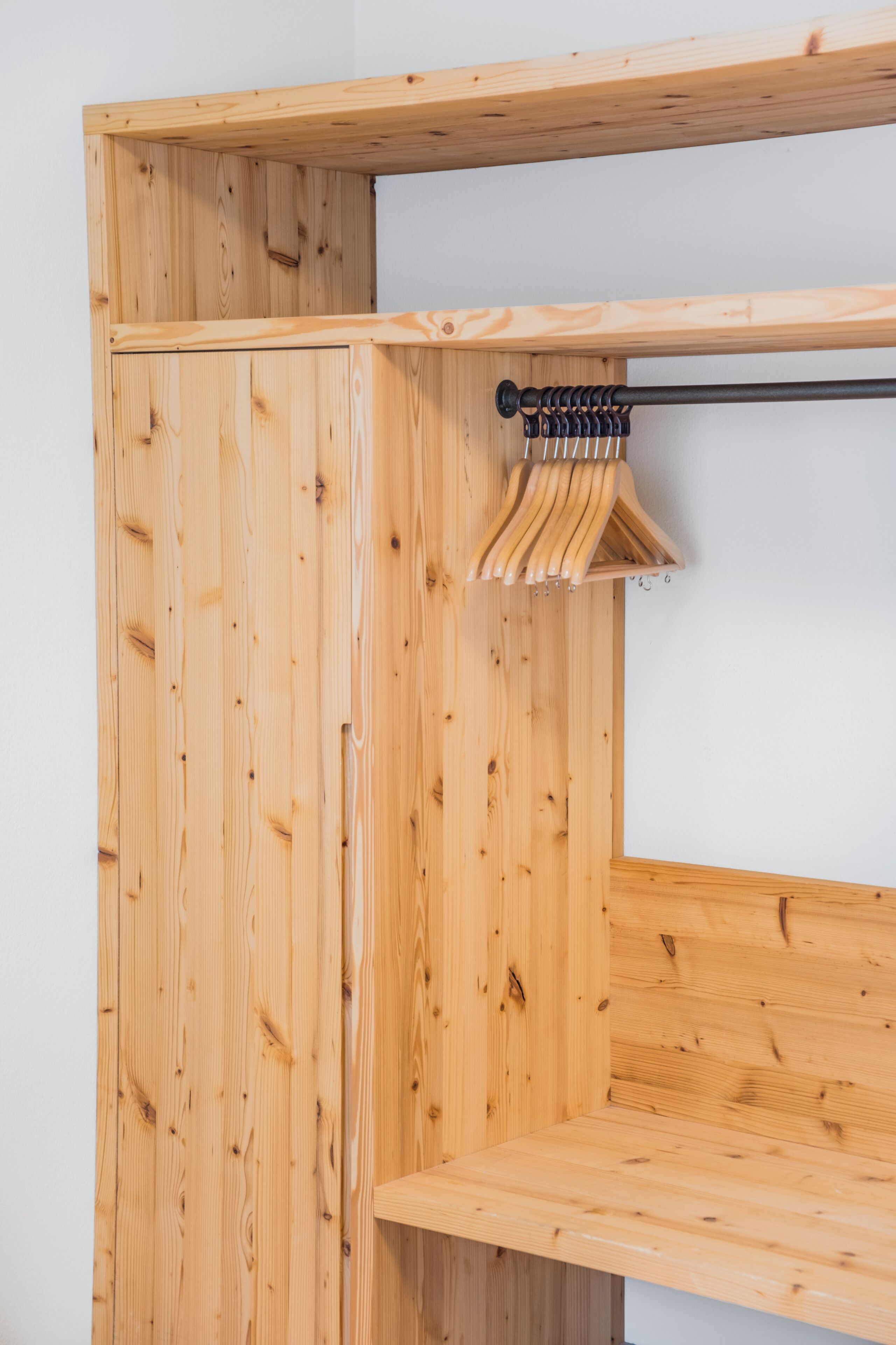 A wooden wardrobe with a hanging rod and a bench.