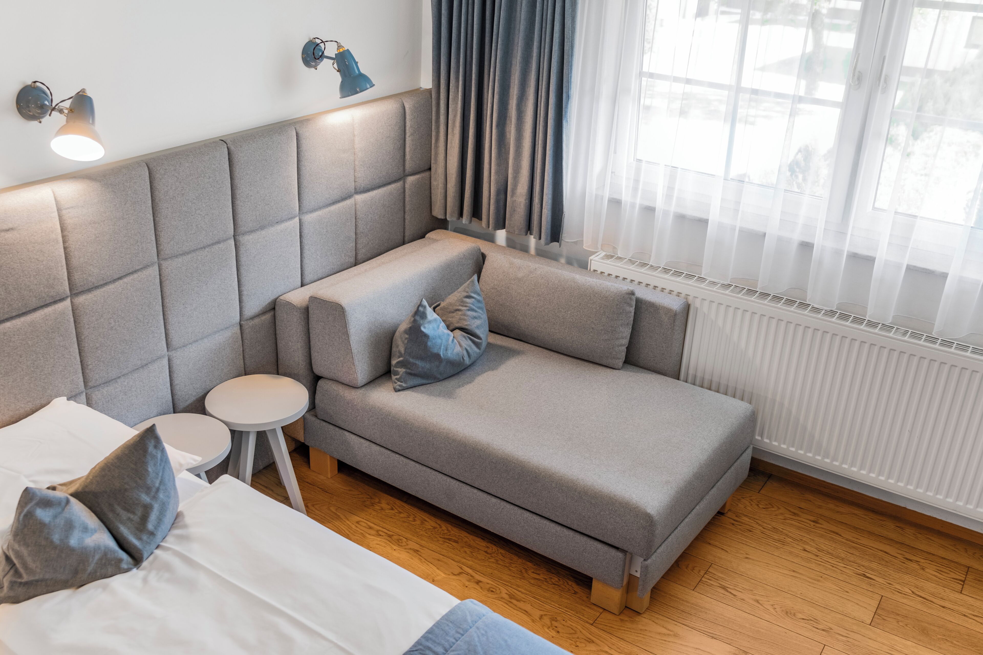A modern hotel room with a sofa, a small round table, a bed, and a radiator.