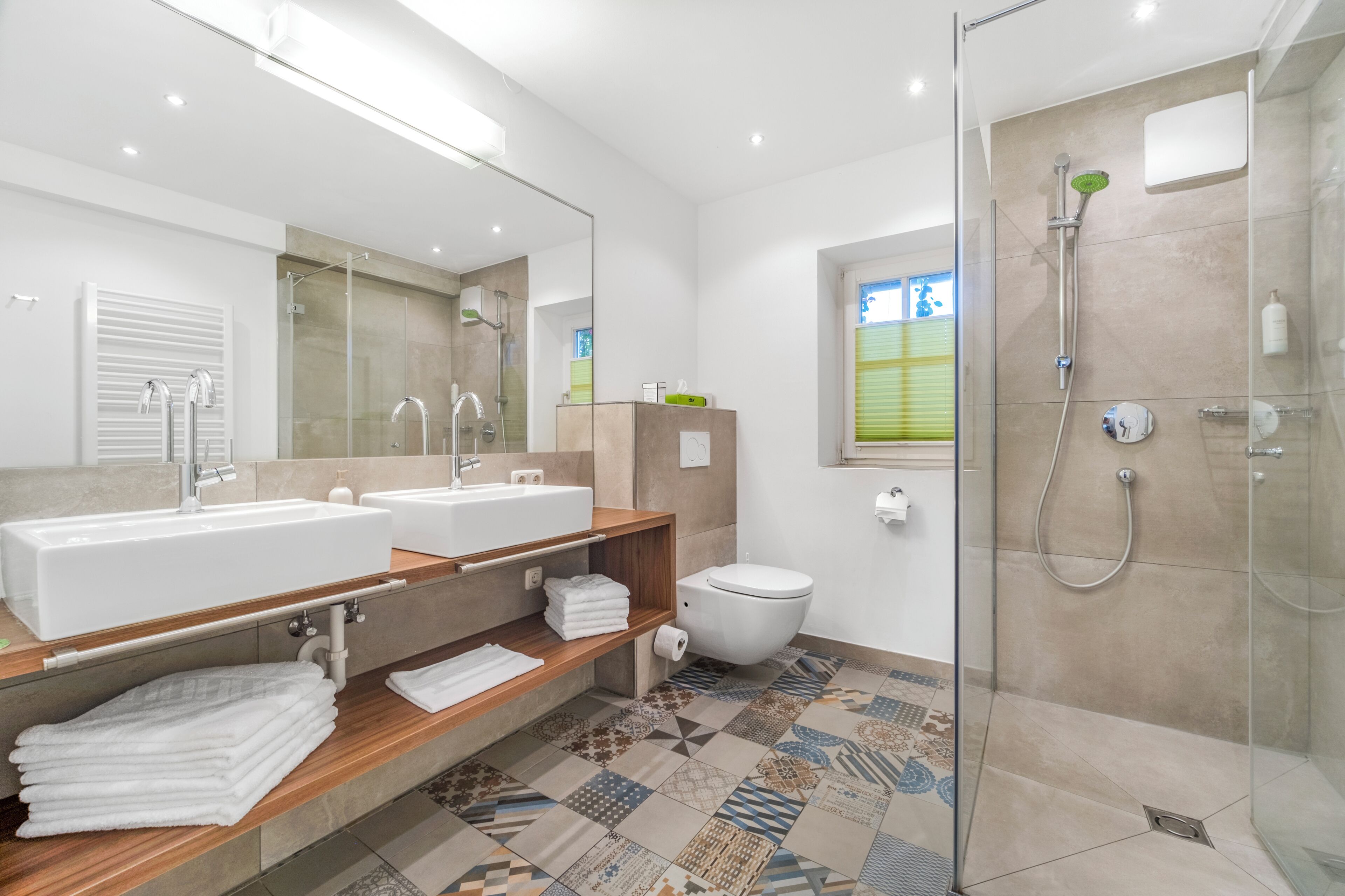 Une salle de bain moderne avec un grand miroir, deux vasques, des toilettes et une douche à parois de verre.