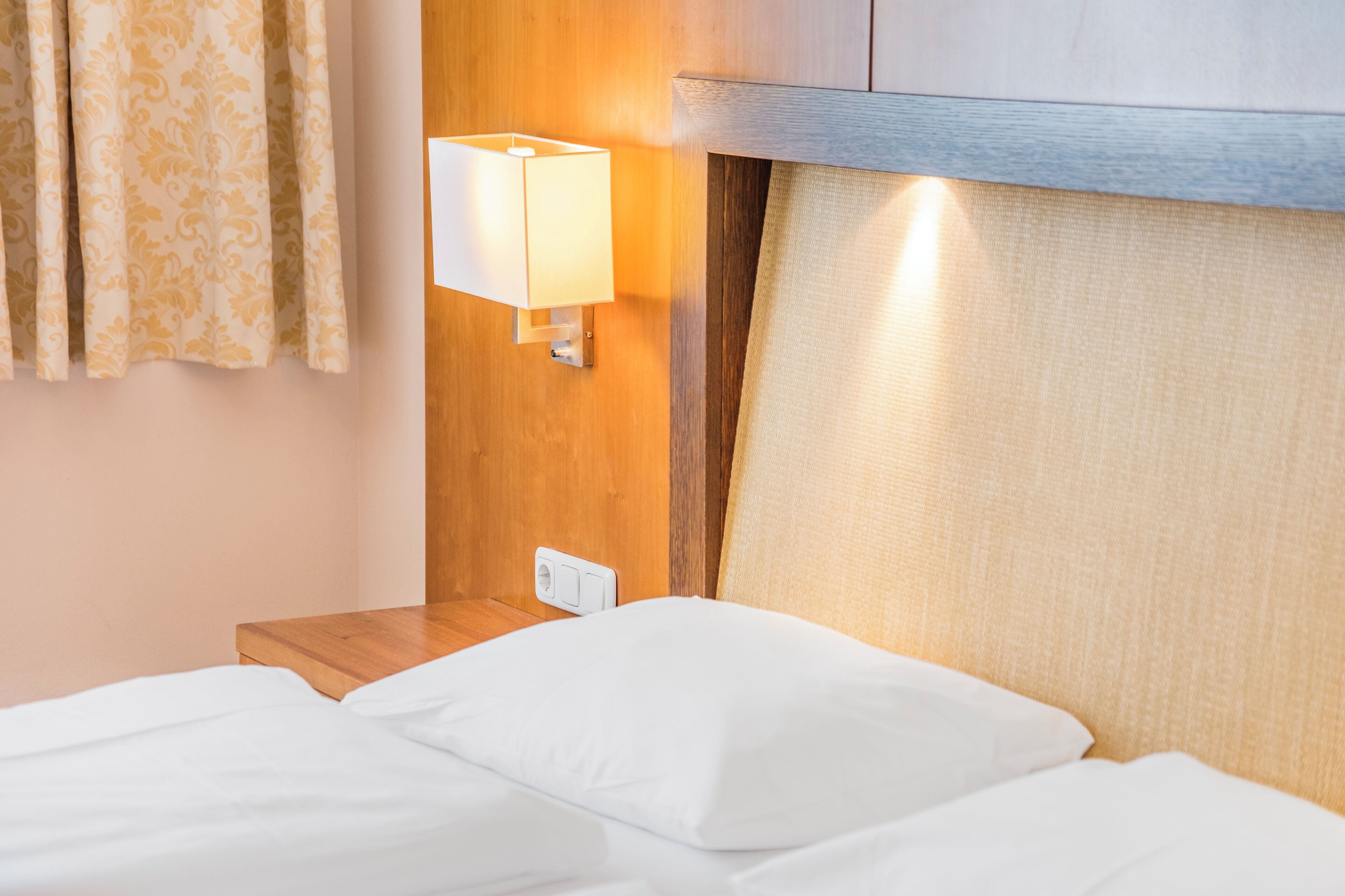 Une chambre d’hôtel avec un lit, une table de chevet, une lampe fixée au mur et une tête de lit en bois.