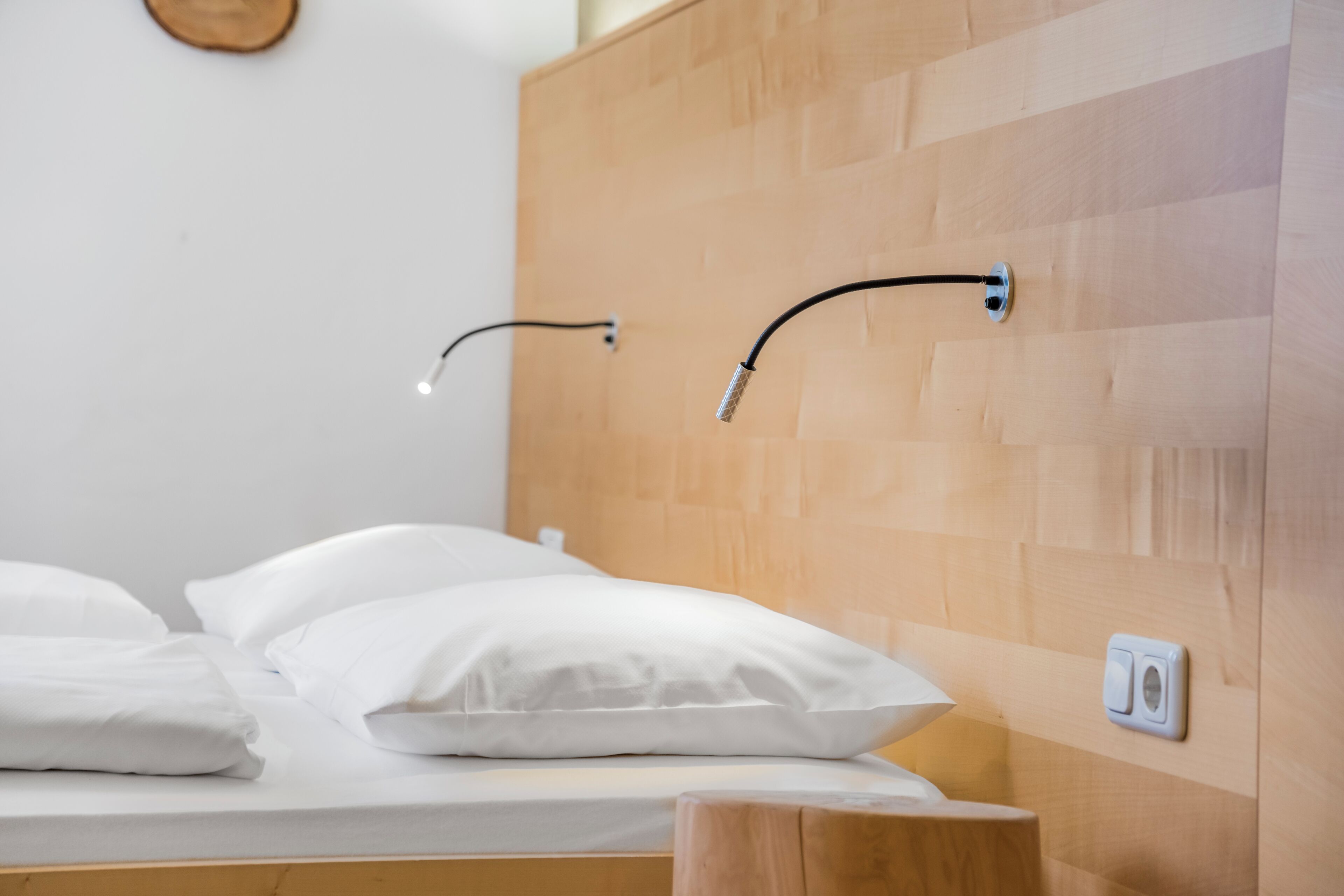 Un letto con biancheria bianca, una testiera in legno e un punto luce a parete.