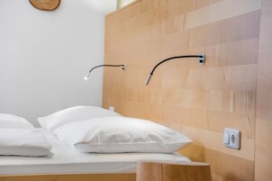 Un letto con biancheria bianca, una testiera in legno e un punto luce a parete.