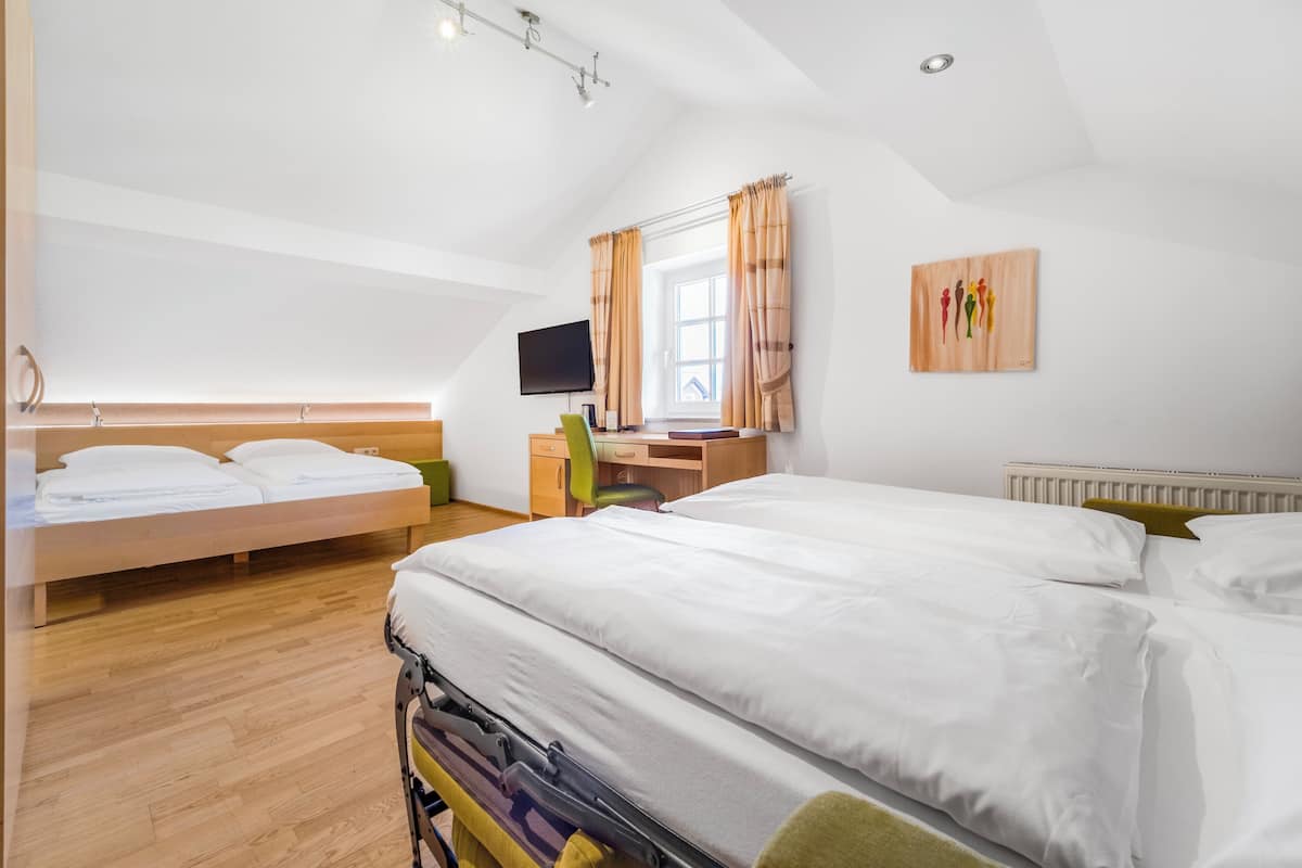 Quarto com duas camas, uma escrivaninha, uma cadeira, uma televisão e uma janela com cortinas.