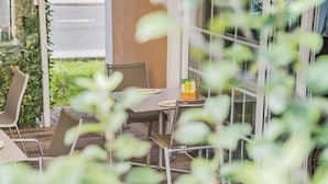 An outdoor seating area with metal chairs and tables, a glass partition, and a small table with a fruit basket. - Das Grüne Hotel zur Post (Salzburg)