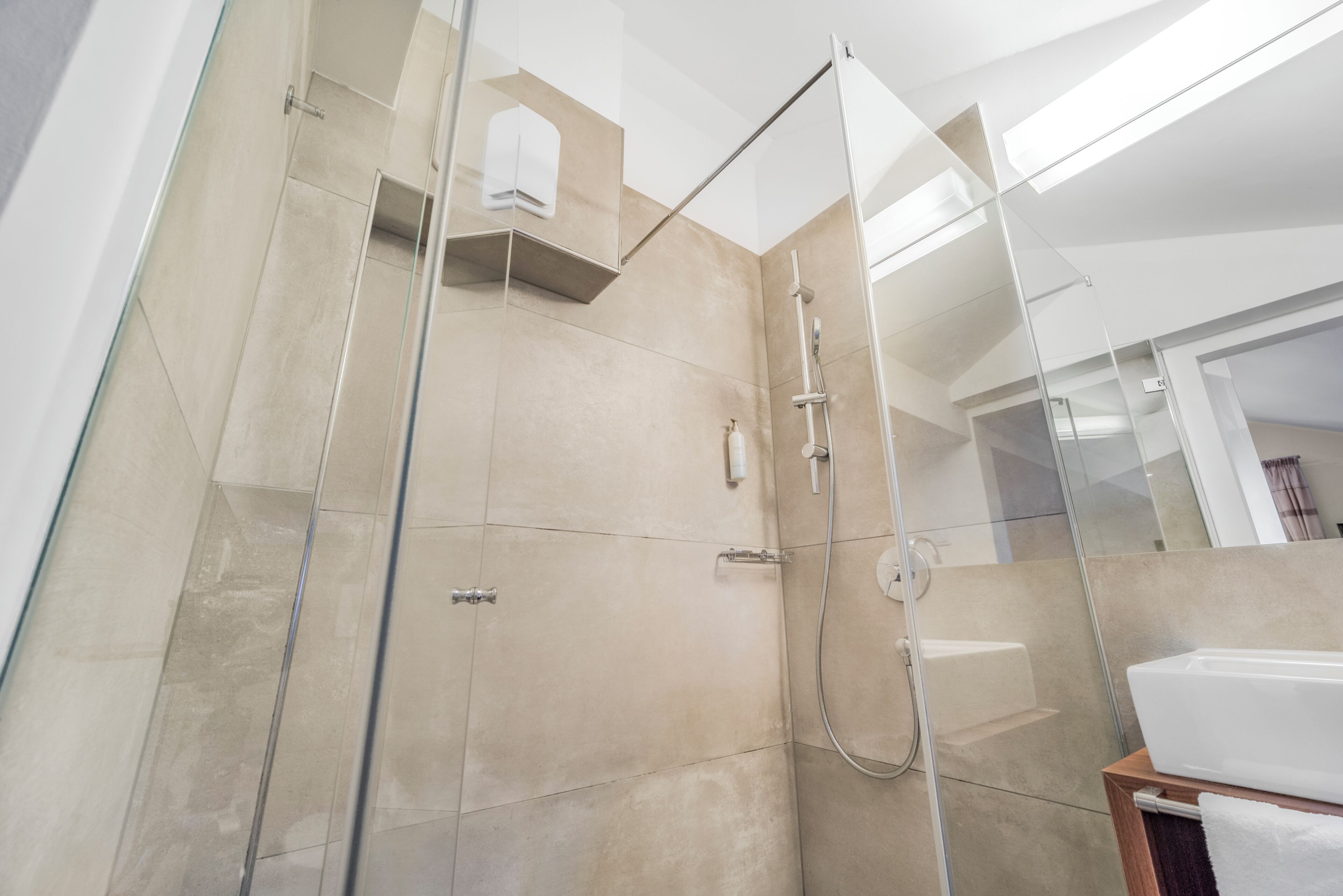 A modern shower area with glass doors, a handheld showerhead, and a wall-mounted control panel.
