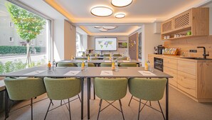 A modern conference room with a long table, green chairs, and a presentation screen. - Das Grüne Hotel zur Post (Salzburg)
