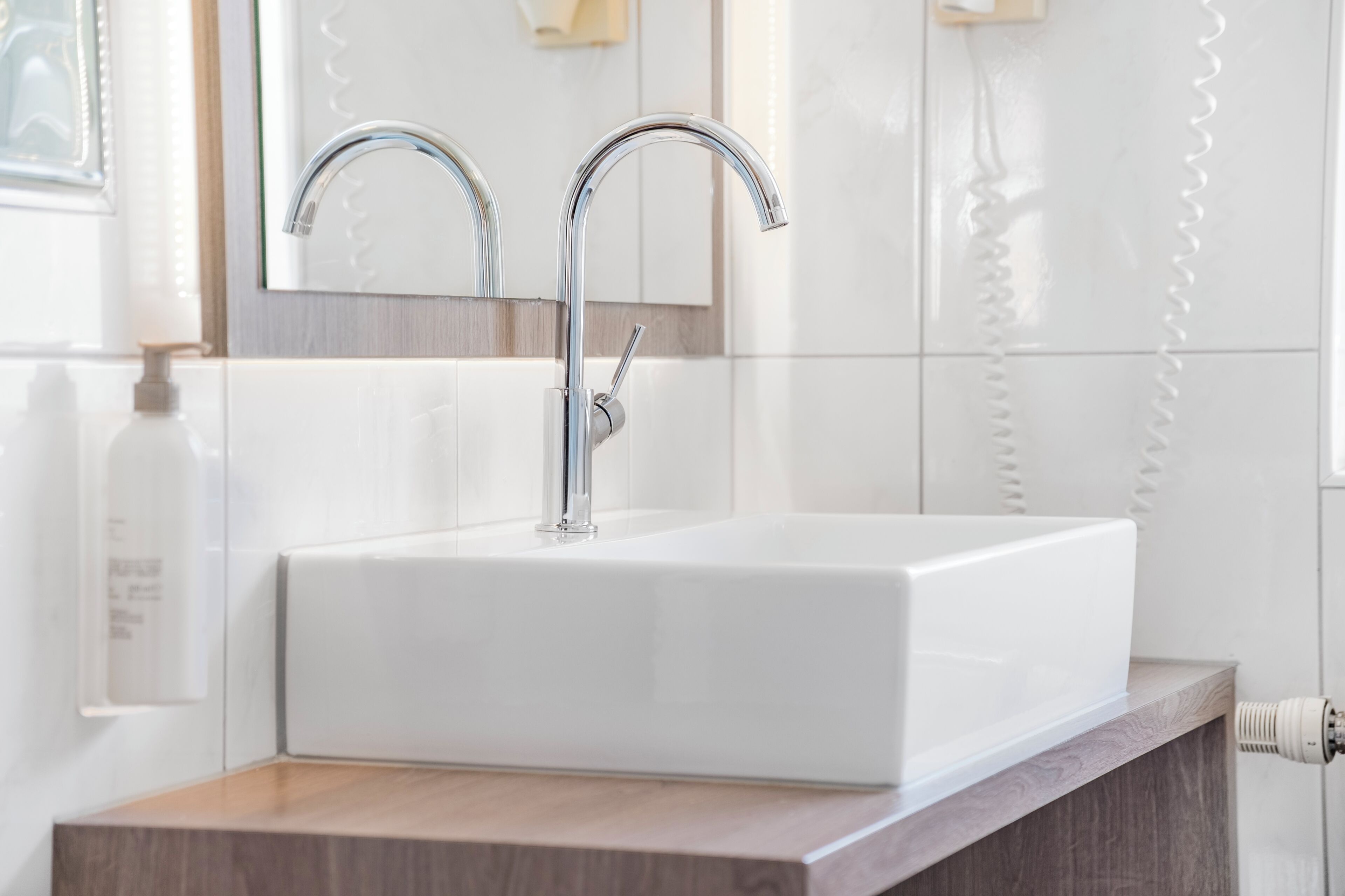 A white bathroom sink with a modern faucet, a wooden countertop, and a mirror above it.