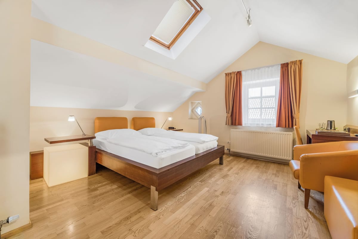 Quarto com cama, mesas de cabeceira, escrivaninha, cadeira, radiador e janela com cortinas.