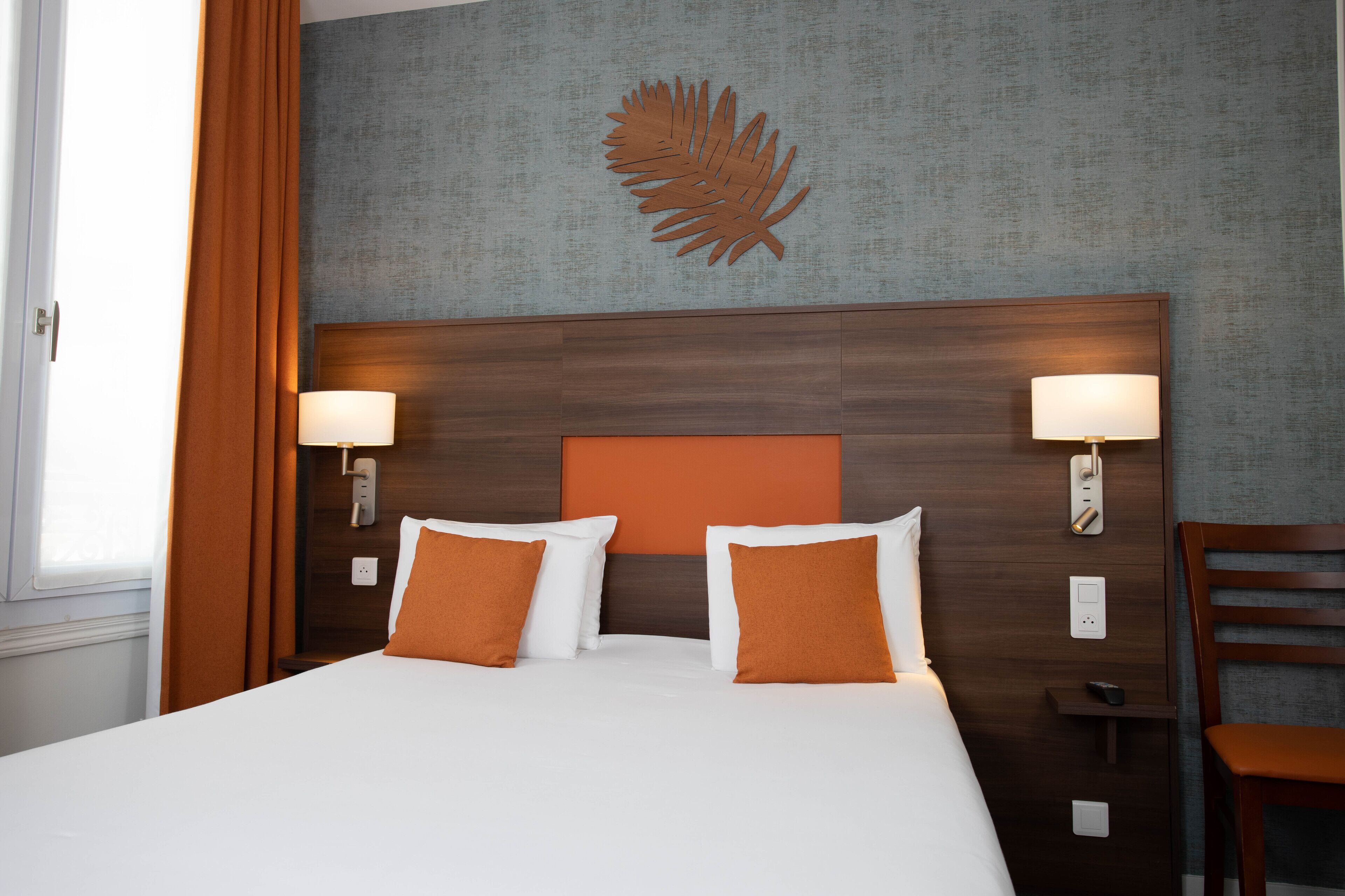 Quarto de hotel com uma cama grande, duas luminárias de cabeceira, uma cabeceira de madeira e um ornamento de parede em formato de folha.