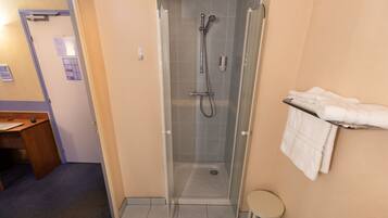 A bathroom with a glass-enclosed shower, a small stool, and a towel rack.