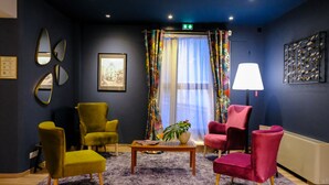 Una habitación con alfombra púrpura, una mesa de centro de madera con revistas y una planta, y cuatro sillas en amarillo, verde, rojo y rosa.