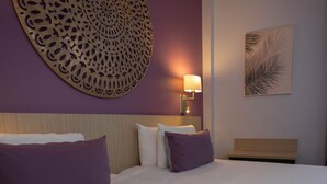 Una habitación de hotel con dos camas, un gran elemento decorativo en la pared, una lámpara fijada a la pared y un cuadro enmarcado.